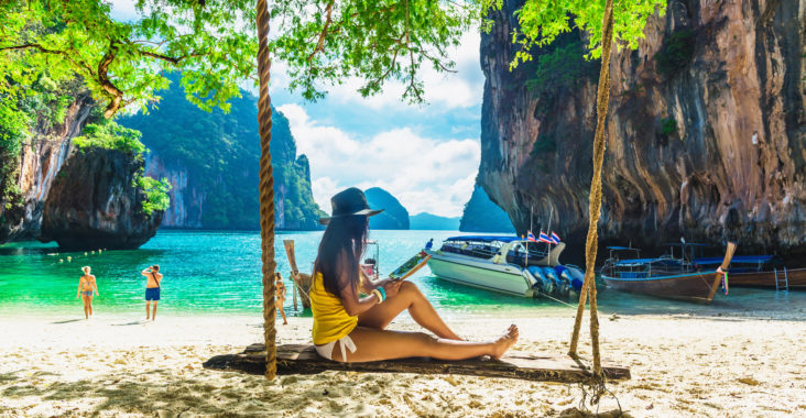 femme assise sur une balançoire et lisant un livre sur une plage en Thaïlande
